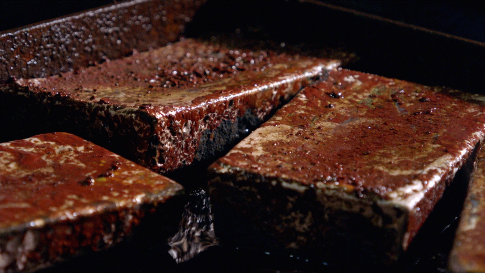 Three freshly-poured gold bars start the cooling process side-by-side, a red powdery residue coats each one.