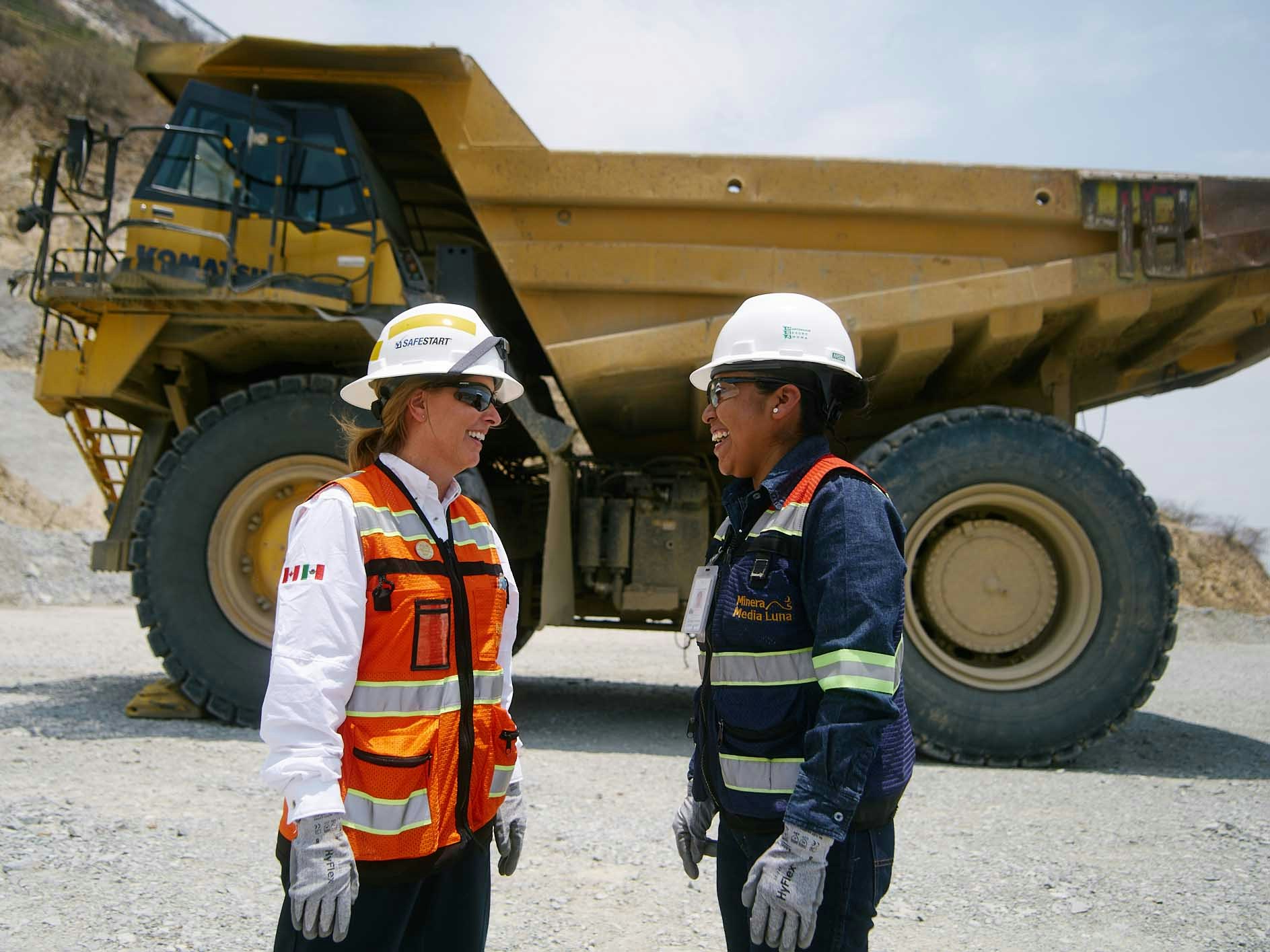Two women facing each other in front of a very large mining truck.
