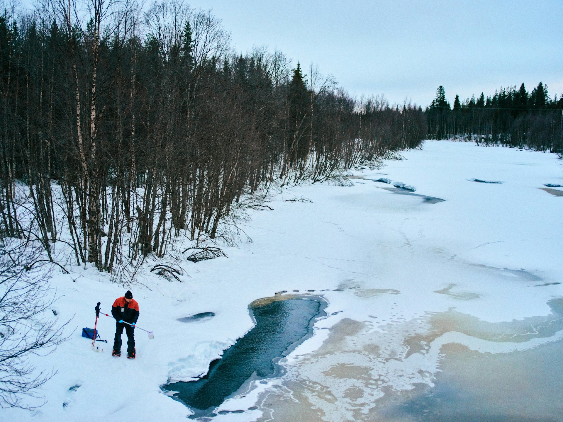 Man standing on frozen lake next to ice hole