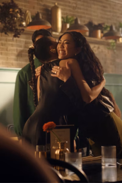 Two people embracing in a busy bar, behind text 'Gold over the long and short term'